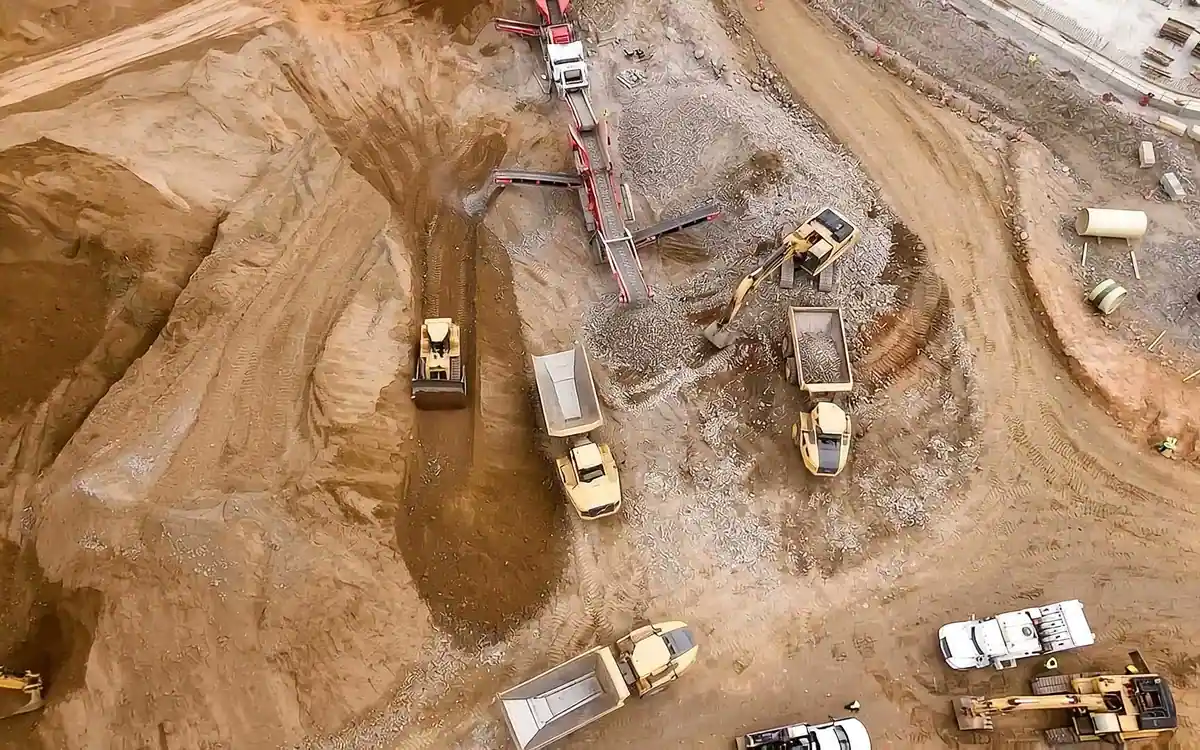 Vista aérea de una obra en operación: excavadoras, camiones de volteo y cribadora